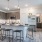 The kitchen area of an apartment, furnished with stainless steel appliances, tall cabinets, vinyl flooring, an island, and a high ceiling